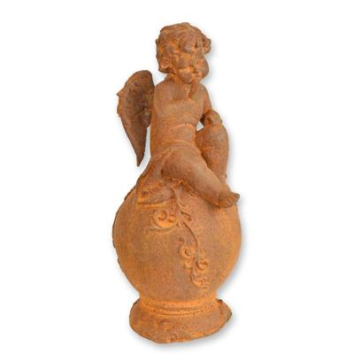A RUSTY CAST IRON FIGURINE OF A PUTTO SITTING ON BALL
