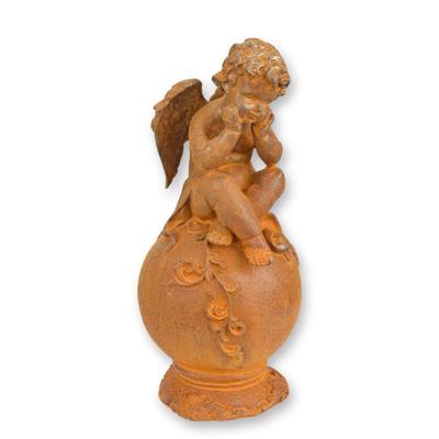 A RUSTY CAST IRON FIGURINE OF A PUTTO SITTING ON BALL